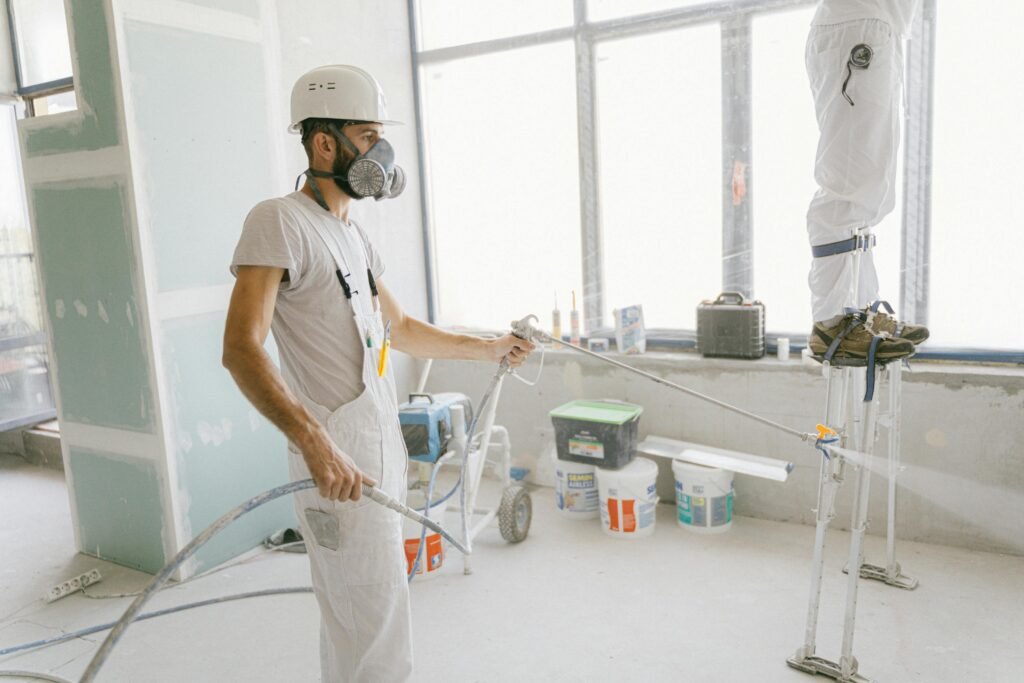Two construction workers wearing protective gear and painting interior walls for a renovation project.